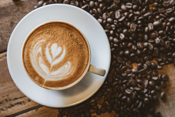 A cup of coffee with heart pattern in a white cup on wooden background