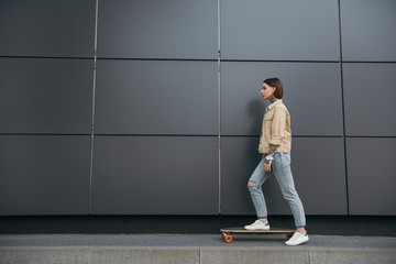 side view of tattooed woman standing with skateboard against black wall