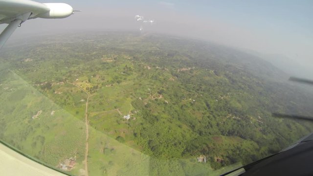 View out the window of prop plane flying over Uganda fields and farms