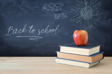 back to school concept. stack of books over wooden desk in front of blackboard.