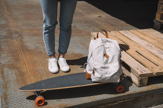 cropped image of woman standing near backpack and skateboard