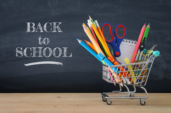 Shopping cart with school supply in front of blackboard. Back to school concept.