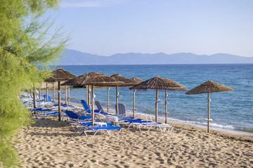 Ierissos beach with loungers under palm tree leaves umbrellas