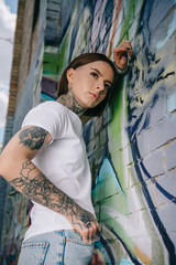 low angle view of stylish tattooed girl posing near wall with colorful graffiti