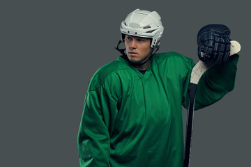 Hockey player wearing green protective gear and white helmet standing with the hockey stick. Isolated on a gray background.