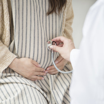 妊婦のお腹に聴診器をあてる女医の手元