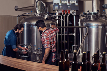 Two bearded hipster males in an apron working in a brewery factory.
