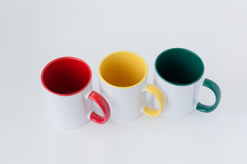 Three white mugs, with a green, yellow, red handle on a light background.  View from above.