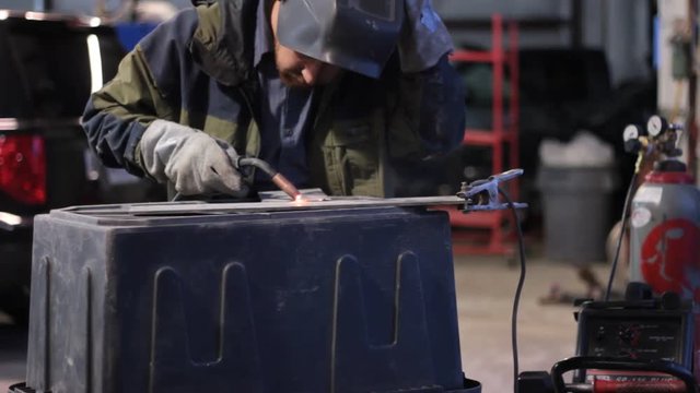 A worker welds a piece of cold rolled steel on top of a work bench.