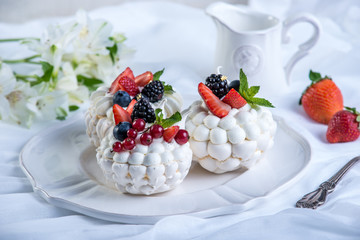 Delicate white meringues with fresh berries on the plate. Dessert Pavlova. Festive wedding cake.