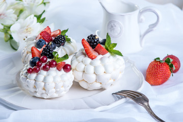 Delicate white meringues with fresh berries on the plate. Dessert Pavlova. Festive wedding cake.