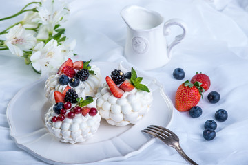Delicate white meringues with fresh berries on the plate. Dessert Pavlova. Festive wedding cake.