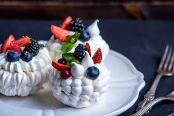 Delicate white meringues with fresh berries on the plate. Dessert Pavlova. Dark background. Wedding cake.