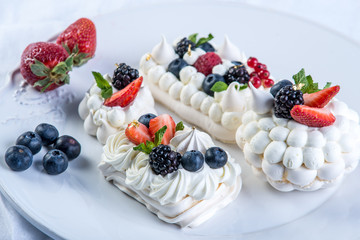 Delicate white meringues with fresh berries on the plate on white background. Dessert Pavlova close-up. Wedding cake.