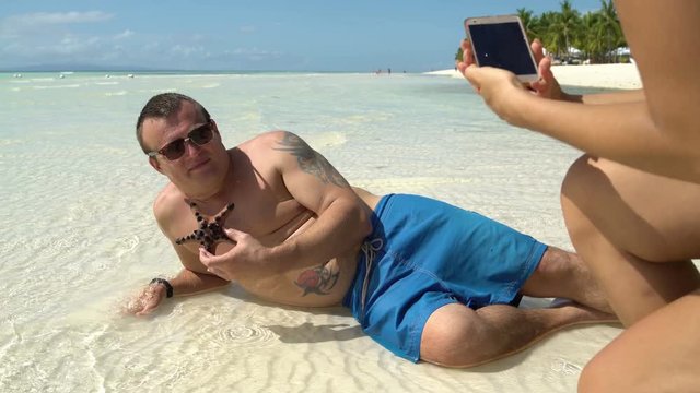 A woman is taking pictures of a man with a starfish on a smartphone