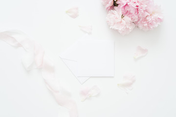 Flat lay, Minimal woman's desktop with blank page mock up, envelope, peony flower with petals, pale pink silk ribbon.