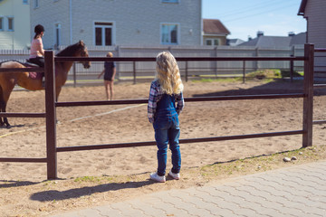 back view of kid looking at mother riding horse at farm