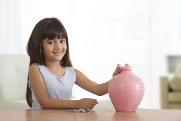 Obraz na płótnie Canvas Portrait of little girl inserting coins in clay piggy bank