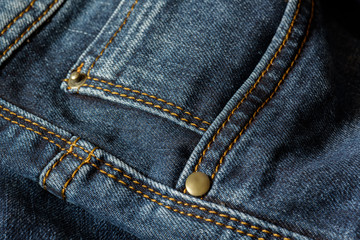 Close-up of a piece of blue jeans with orange stitches. Pocket with rivets close-up.