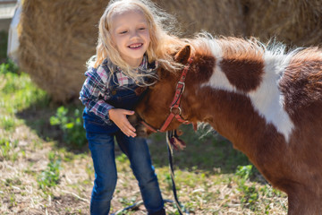 adorable smiling kid touching cute pony at farm