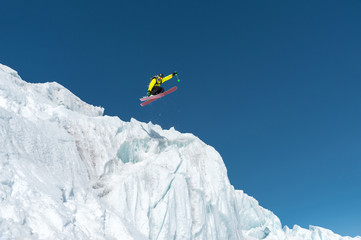 A jumping skier jumping from a glacier against a blue sky high in the mountains. Professional skiing