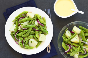 Green bean, potato and red onion salad with parsley, hollandaise sauce on the side, photographed overhead on slate with natural light