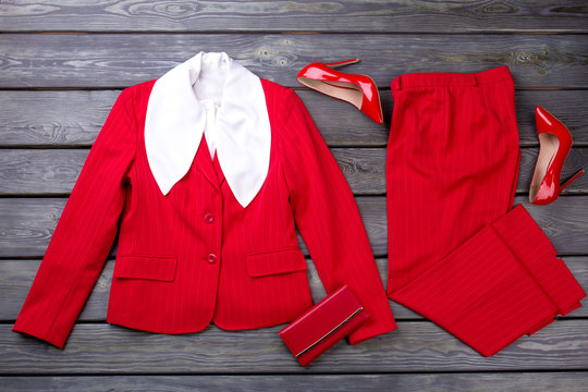 Red women's formal business clothes and accessories. Flat lay, grey wooden surface background.