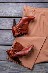 Pair of high heel leather shoes. Brown women's trousers. Grey wooden surface background.