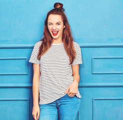 Young stylish girl model in casual summer clothes with red lips, posing near blue wall. Winking