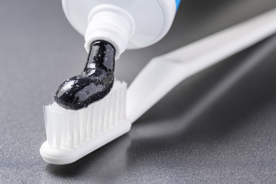 Black charcoal toothpaste being squeezed on white toothbrush