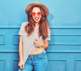 Young stylish girl model in casual summer clothes and brown hat with red lips, posing near blue...