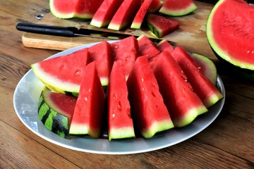 Watermelon slices on a plate, cutting board with watermelon pieces on a background.