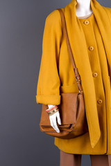 Mannequin with coat and handbag. Braceletes on dummy hand. Black background.