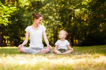 Mom and son are practicing yoga in the park.