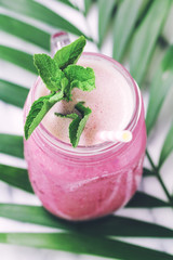 Fruit pink smoothie in a glass jar on a palm leaf. Minimalist style. Trend vintage toned.