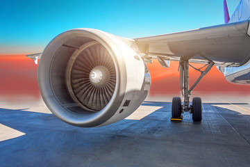 Aircraft jet engine close-up, airplane wing and chassis of landing gear wheel parked at the airport on a sky clouds background.