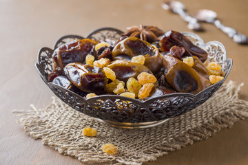 Oriental sweets, dried fruit dates and raisins, cinnamon and star anise in a plate on a wooden background.