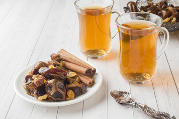 Oriental sweets, dried fruit dates and raisins, cinnamon and star anise in a plate. Turkish tea in glasses on a wooden background.