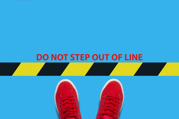 Legs in red sneakers on a blue background with a restrictive yellow black stripe with text Do not...