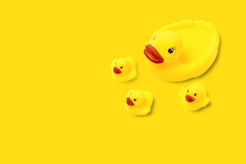 Rubber toy of yellow color Mama duck and small ducklings on a yellow background. The concept of maternal care and love for children. Flat lay, top view