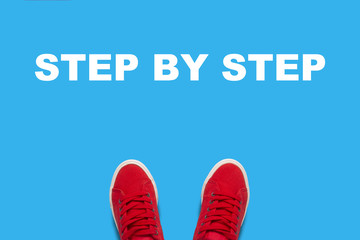 Legs in red sneakers standing on a blue background with text Step by step. Concept of the sequence of actions. Flat lay, top view