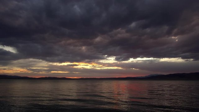 Dramatic clouds reflecting in Utah Lake at sunset as you hear the sound of the water ripple on shore.