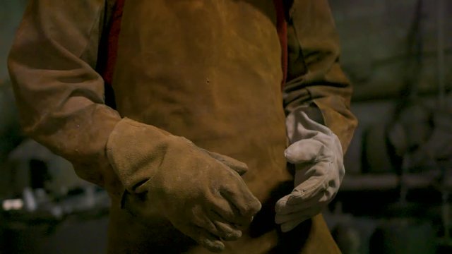 Epic footage of a speed-ramped clip, showing a metal worker putting on leather gloves.