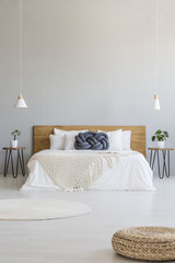 Pouf in spacious grey bedroom interior with lamps above bed with blue pillow. Real photo