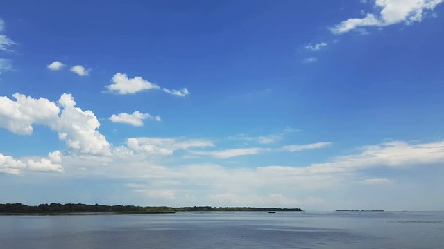 Colorful spring summer landscape on river with beautiful clouds in the sky, shooting from a car that goes on the road along the water, dynamic scene, 4k video.