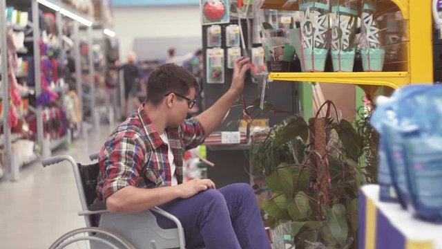 Man salesman with a disability in a wheelchair puts the goods on the shelves in the store