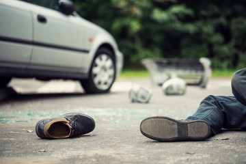 Close-up of a shoe lying next to a car crash victim with a blurred car in the background