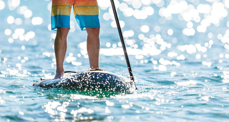 Detail of young man standing on paddleboard.