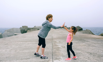 Senior sportswoman and little girl high five by sea pier