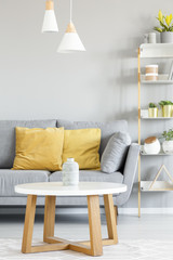 Lamps above wooden table in front of grey sofa with yellow pillows in apartment interior. Real photo